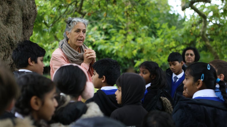 Artist Jasmin Bhanji and a group of children in discussion, surrounded by the greenery of the garden at Osterley Park
